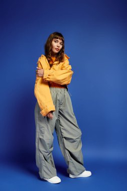 Genç bir kadın kendine güvenerek poz veriyor, şık ve canlı renklerde spor kıyafetleri giyiyor..