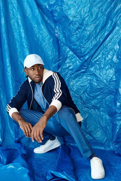 Çekici bir gülüşü olan genç bir adam, kendine güvenen mavi elbiseli, modaya uygun bir poz verir..