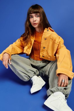 Genç bayan kendine güvenerek oturuyor, gösterişli kıyafetlerini ve eşsiz tarzını maviye karşı sergiliyor..