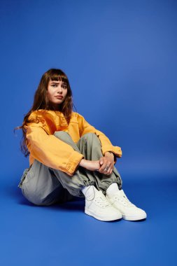 Canlı bir pozda oturan şık giyinmiş genç bir kadın kendine güven ve tarz saçar..