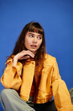 Şık bir genç kadın kendine güvenerek poz veriyor. Şık, mavi bir arka planı var..