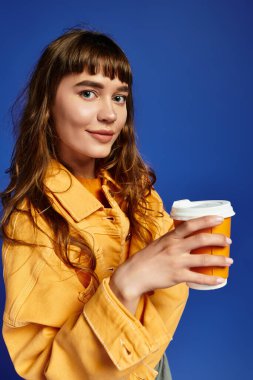 Dalgalı saçlı genç bir kadın içki tutuyor, şık bir şekilde poz veriyor ve neşe saçıyor..