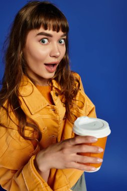 Modaya uygun genç bir kadın elinde neşeli bir ifadeyle bir kahve fincanı tutuyor..