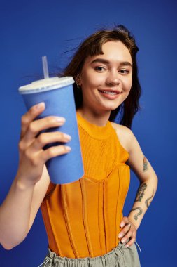 Moda kıyafetli genç bir kadın elinde renkli bir içki tutarken gülümsüyor..