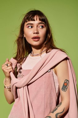 Kendine güvenen, modaya uygun giyinmiş genç bir kadın canlı yeşil bir arka plana karşı poz veriyor..