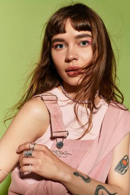 Tarz sahibi genç bir kadın canlı yeşil bir arka plana karşı özgüvenle poz verir..