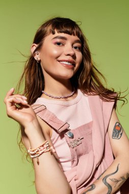 Parlak bir gülüşü olan şık bir genç kadın yeşil bir zemine karşı şık kıyafetini sergiliyor..