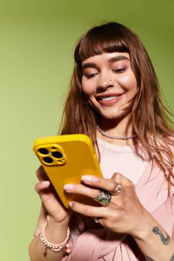 Genç, modaya uygun bir kadın telefonuna bakarken neşeyle gülümser, şık kıyafetler giyer..