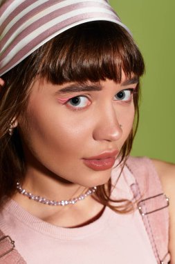 Genç bir kadın neşeli bir saç bandıyla şık kıyafetler giyiyor ve hareketli bir ortamda makyaj yapıyor..