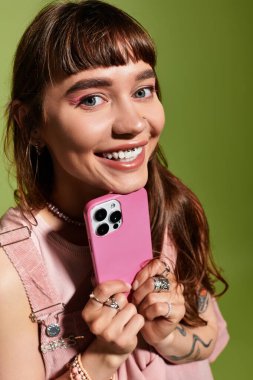 Çekici bir gülümsemesi olan genç bir kadın, şık bir anın tadını çıkarırken cep telefonu cihazını gösteriyor..