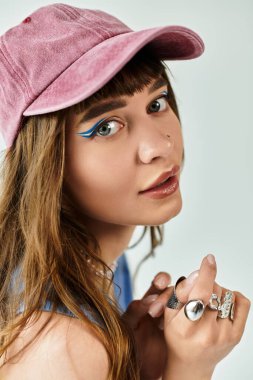 Moda şapkalı kendine güvenen genç bir kadın canlı göz makyajını ve şık yüzüklerini ön plana çıkarıyor..