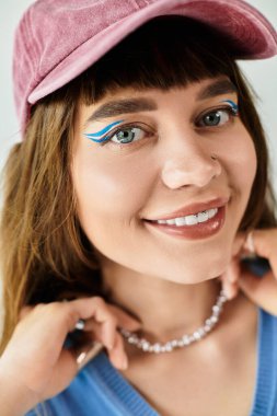 Parlak gözlü kadın kolyesini düzeltirken ve tarzını gösterirken son moda tebessümlerle gülümsüyor.