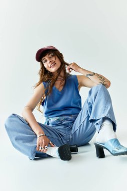 Şık genç bir kadın yerde oturuyor, benzersiz modasını ve neşeli ruhunu sergiliyor..