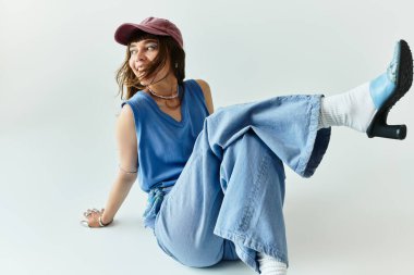 Şık, genç bir kadın gündelik bir şekilde oturup şık kıyafetlerini ve parlak gülümsemesini sergiliyor..