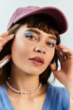 Çarpıcı mavi göz kalemi olan genç bir kadın şık aksesuarlarını düzeltirken kendine güvenerek poz veriyor..