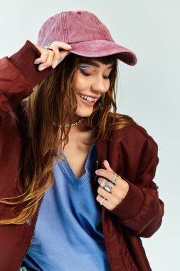 Genç, şık bir kadın şapkasını düzeltirken, şık kıyafetini sergilerken neşeyle gülümsüyor..