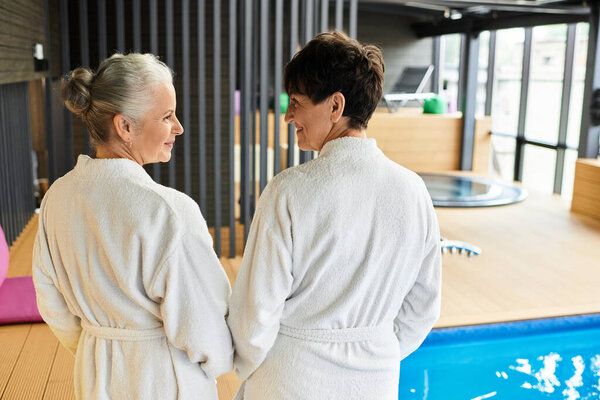 Two beautiful mature women relax and share smiles at a wellness center for active seniors.