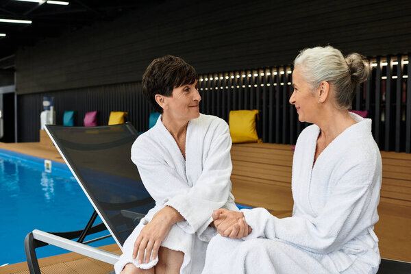 Two beautiful mature women relax in cozy robes, cherishing their time at the wellness center.