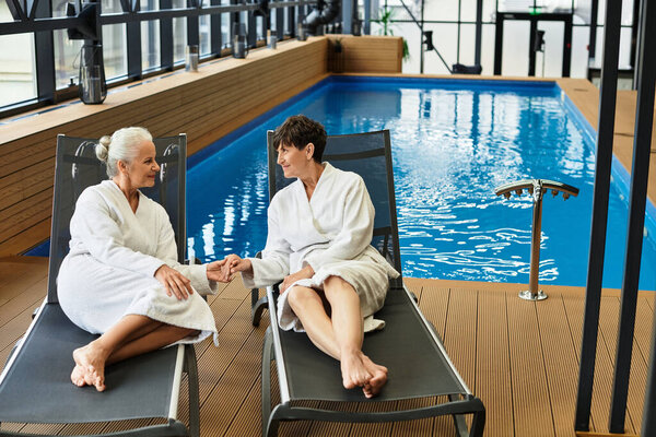 Two beautiful mature women share a peaceful moment at a wellness center by the pool.