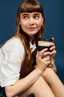 Uzun saçlı, gülümseyen genç bir kadın bir kahve fincanı tutuyor. Çalışma saatlerinde düşüncelere dalmış..