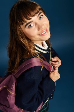 Sırt çantalı kendine güvenen genç bir kız öğrenci parlak mavi bir arka plana karşı duruyor..