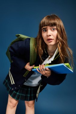 Sırt çantası ve kitapları olan güzel bir kız öğrenci renkli bir ortamda merak gösteriyor..