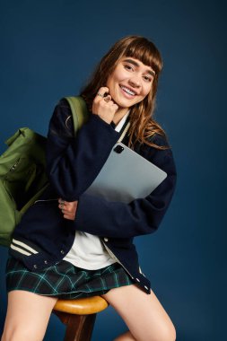 Mutlu genç kız öğrenci bir tablet tutuyor ve sıcak, davetkar bir ortamda gülümsüyor..