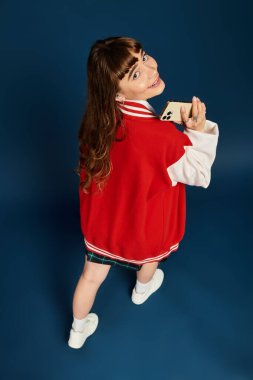 Neşeli bir öğrenci telefonuyla gülümsüyor, çalışma sırasında canlı bir ceket giyiyor..