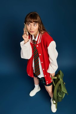 Kırmızı ceketli genç bir kız telefonuyla havalı bir mavi arka planda konuşuyor..