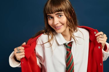 Genç bir kadın neşe içinde şık kırmızı ceketini beyaz bir gömlek ve kravatın üzerine çıkarıyor..