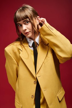 Genç bir kadın şık, sarı bir ceketle şık bir şekilde poz veriyor, zarifliğini ve çekiciliğini sergiliyor..