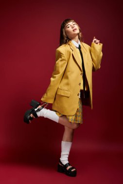 Neşeli bir öğrenci zengin kırmızı bir arkaplana karşı duruyor, şık bir kıyafete güveni var..