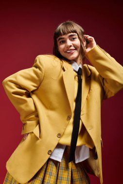 Büyük ceketli ve ekose etekli mutlu bir kız öğrenci kendinden emin bir poz verir..