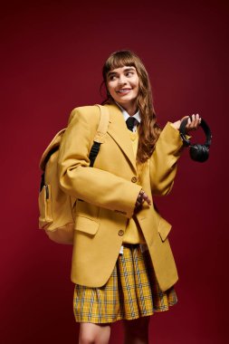 Genç bir kız öğrenci coşkulu bir arkaplan önünde zevkle poz veriyor, eşsiz tarzını gösteriyor..