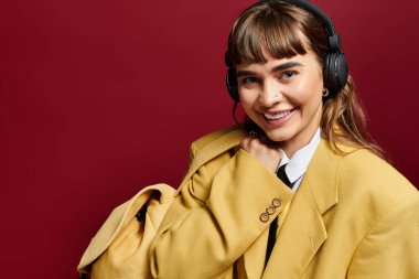 Şık giyinmiş gülümseyen genç kadın, çalışma odasına dalmış bir çanta taşırken kulaklık takıyor..