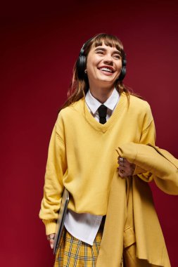 Genç bir kadın kulaklıkla çalışırken neşeli sarı bir kazak ve ekose etek giyiyor..