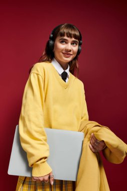 Sarı süveter ve ekose etekli güzel öğrenci elinde bir dizüstü bilgisayar tutuyor, çalışmaya ve yaratmaya hazır..