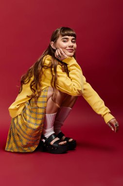 Gülümseyen genç kadın zarif bir şekilde kırmızı arka planda şık bir kıyafet giyiyor..