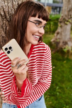 Parkta güzel bir genç kadın gülümser ve akıllı telefonuyla meşgul olur..