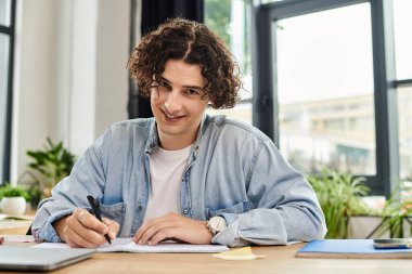 Genç adam, modern çalışma alanını dolduran parlak, bitki dolu bir yerde yazmakla meşgul..
