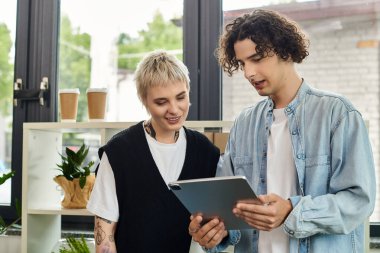 İki genç profesyonel parlak bir ofis ortamında bir tableti incelerken fikirleri tartışıyor.