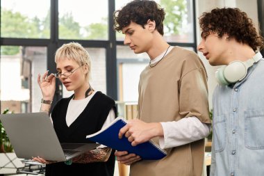 Modern bir ofiste dizüstü bilgisayarla fikirleri ve ilerlemeyi tartışan üç genç profesyonel..