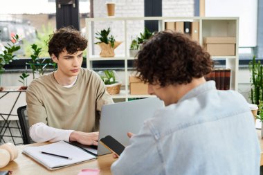Bitkilerle dolu çağdaş bir ofis masasında odaklanmış iki genç insan..