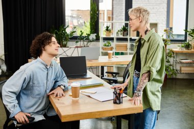 İki genç, doğal ışıkla yıkanmış şık, bitki dolu bir ofiste hareketli bir şekilde sohbet ediyorlar..