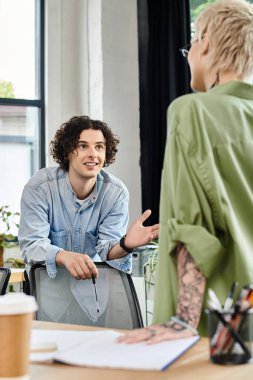İki genç profesyonel, görevleri üzerinde çalışırken parlak bir ofiste etkin bir şekilde sohbet ediyorlar..