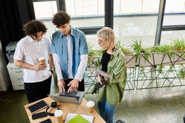 Kendini işine adamış üç genç şık bir ofis alanında dizüstü bilgisayarın etrafında verimli bir tartışmaya girişiyor..