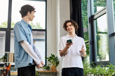 İki genç, yeşillik dolu şık bir ofiste iş hakkında konuşuyor..