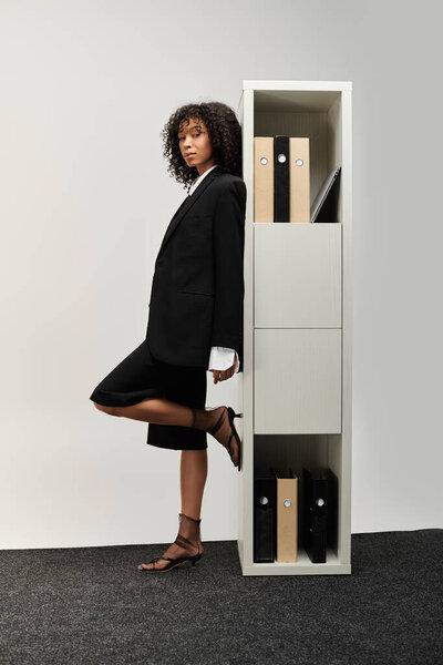 Молодая красивая женщина элегантно позирует в деловой одежде, демонстрируя уверенность и уравновешенность.