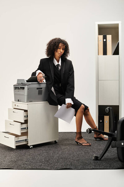 Стильная молодая женщина элегантно сидит в шикарном офисе, излучая профессионализм.