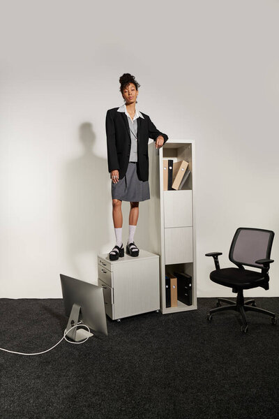 Уверенная молодая женщина стоит на офисных принадлежностях, демонстрируя элегантность в современной рабочей обстановке.